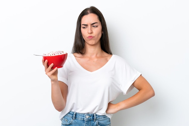 Jeune femme caucasienne prenant du lait de petit déjeuner isolé sur fond blanc avec une expression triste