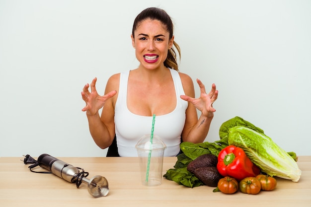 Jeune femme caucasienne, préparer un smoothie sain avec des légumes hurlant de rage.