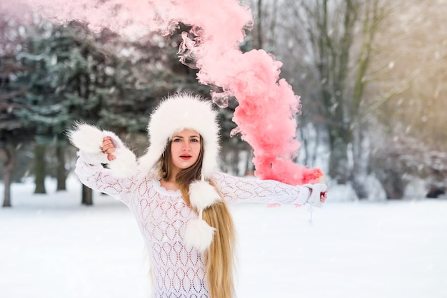 Jeune femme caucasienne en pull avec bombe fumigène rouge le jour de l'hiver neige