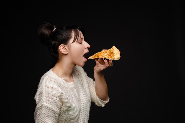 Jeune femme caucasienne avec queue manger un morceau de pizza.