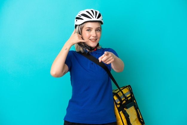 Jeune femme caucasienne avec sac à dos thermique isolé sur fond bleu faisant un geste de téléphone et pointant vers l'avant