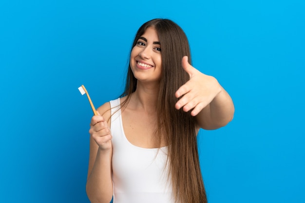 Jeune femme caucasienne se brosser les dents isolées sur fond bleu se serrant la main pour conclure une bonne affaire