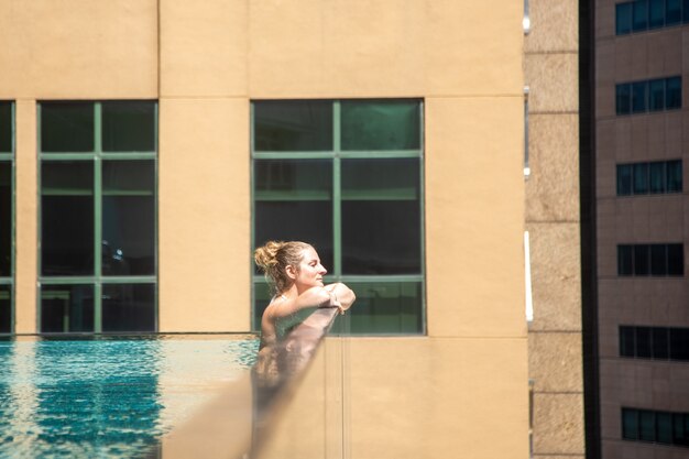 jeune femme caucasienne se détendre dans une piscine sur le toit d'un gratte-ciel dans une métropole sous le soleil....