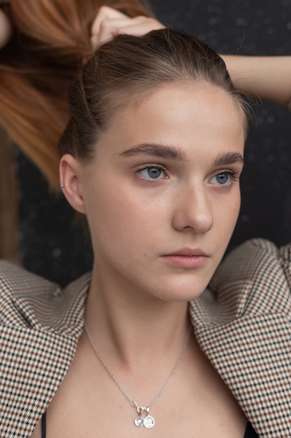 Jeune femme caucasienne séduisante aux cheveux longs, yeux bleus en costume recueillant ses cheveux en queue de cheval