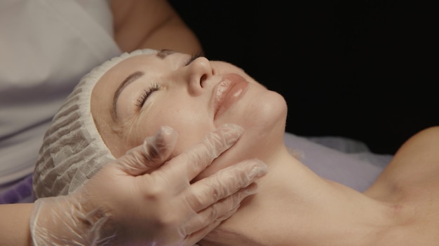 Jeune femme caucasienne séduisante recevant un massage facial anti-âge dans un salon de spa relaxant sur une table de massage. Soins de bien-être du corps et de la peau, soins de beauté du visage, procédure de rajeunissement