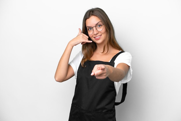 Jeune femme caucasienne de serveur de restaurant isolée sur fond blanc faisant un geste de téléphone et pointant vers l'avant