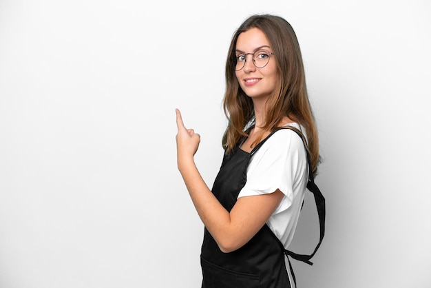 Jeune femme caucasienne de serveur de restaurant isolée sur fond blanc pointant vers l'arrière