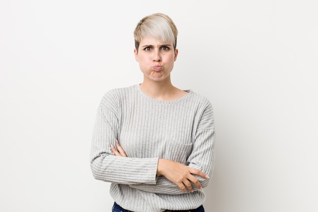 Jeune femme caucasienne sinueuse isolée sur blanc souffle les joues, a fatigué l'expression. Expression faciale.