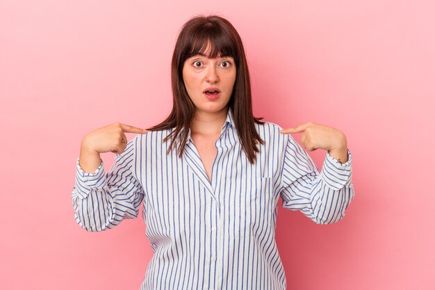 Jeune femme caucasienne sinueuse isolée sur fond rose pointe vers le bas avec les doigts, sentiment positif.