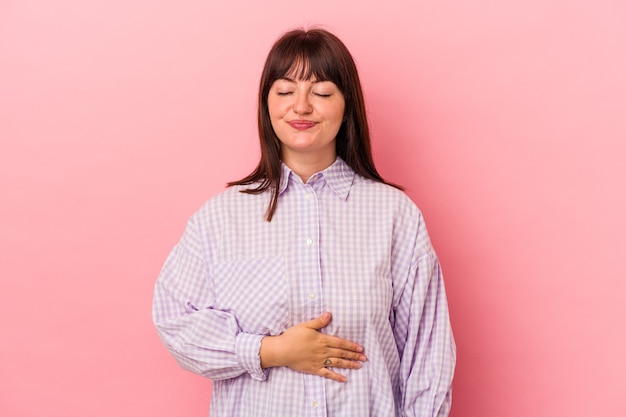 Jeune femme caucasienne sinueuse isolée sur fond rose touche le ventre, sourit doucement, mange et satisfait le concept.