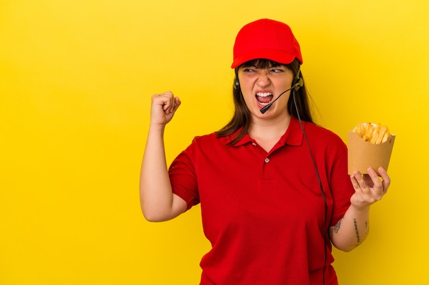 Jeune femme caucasienne sinueuse travailleur de restauration rapide tenant des frites isolées sur fond bleu levant le poing après une victoire, concept gagnant.