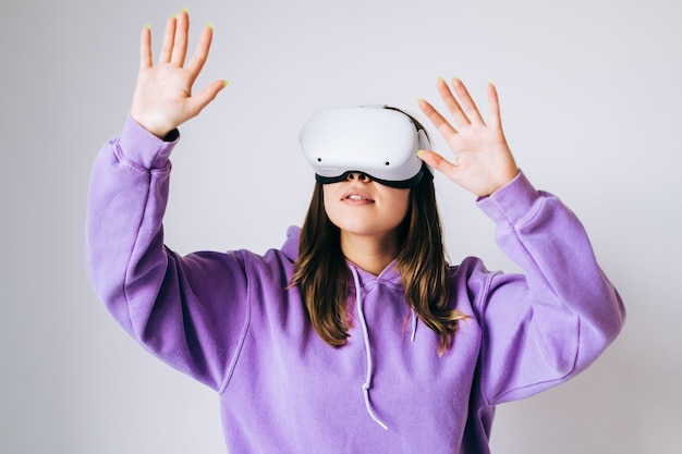 Jeune femme caucasienne souriante à l'aide de casque VR, gesticulant et levant dans la réalité virtuelle.