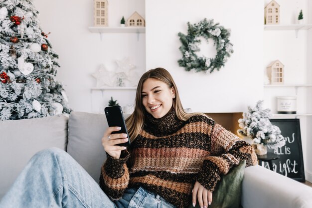 Jeune femme caucasienne souriante à l'aide de téléphone portable en vacances à la maison sur le canapé.