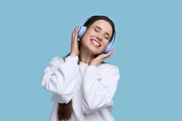 Une jeune femme caucasienne souriante dans un casque écoute des danses de la bande sonore sur fond bleu de musique