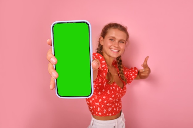 Une jeune femme caucasienne souriante et optimiste tient un téléphone avec un écran vert