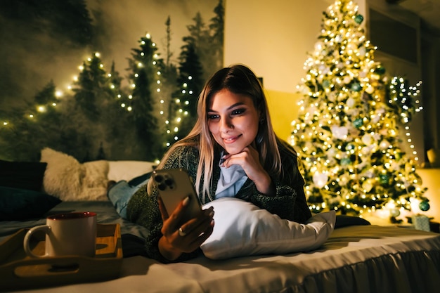 Jeune femme caucasienne souriante utilisant un téléphone portable en vacances à la maison sur le lit.