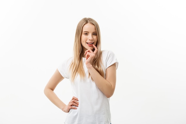 Jeune femme caucasienne avec un sourire timide et ludique adorable mignon. T-shirt blanc modèle isolé sur fond blanc.