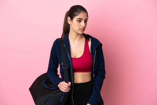 Jeune femme caucasienne de sport avec sac de sport isolé sur fond rose regardant sur le côté