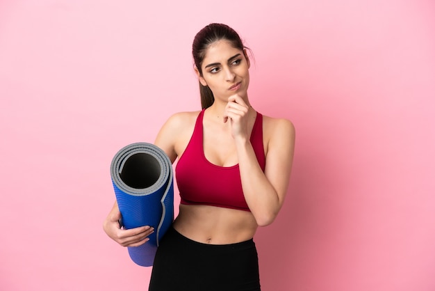 Jeune femme caucasienne sportive allant à des cours de yoga tout en tenant un tapis ayant des doutes