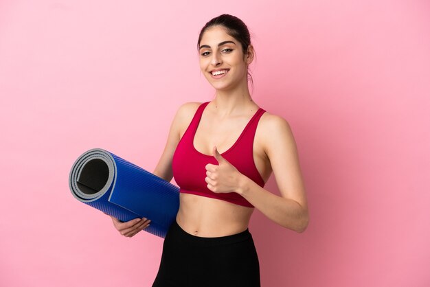 Jeune femme caucasienne sportive allant à des cours de yoga tout en tenant un tapis donnant un geste du pouce levé