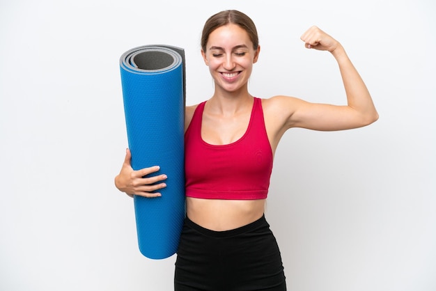 Jeune femme caucasienne sportive allant à des cours de yoga tout en tenant un tapis isolé sur fond blanc faisant un geste fort