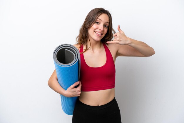 Jeune femme caucasienne sportive allant à des cours de yoga tout en tenant un tapis isolé sur fond blanc faisant un geste de téléphone Appelez-moi signe de retour