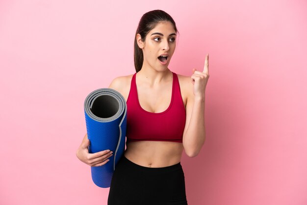 Jeune femme caucasienne sportive allant à des cours de yoga tout en tenant un tapis en pensant à une idée pointant le doigt vers le haut