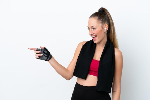 Jeune femme caucasienne sportive isolée sur fond blanc, pointant le doigt sur le côté et présentant un produit