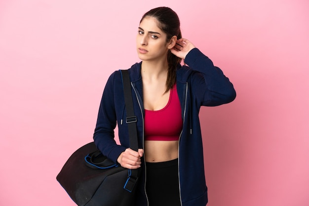 Jeune femme caucasienne sportive avec sac de sport isolé sur fond rose ayant des doutes