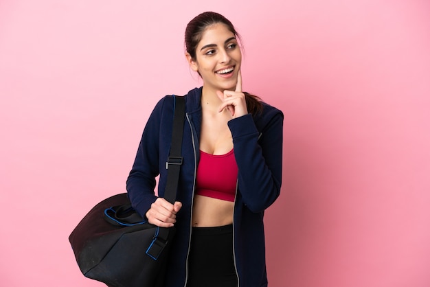 Jeune femme caucasienne sportive avec sac de sport isolé sur fond rose en pensant à une idée tout en levant les yeux