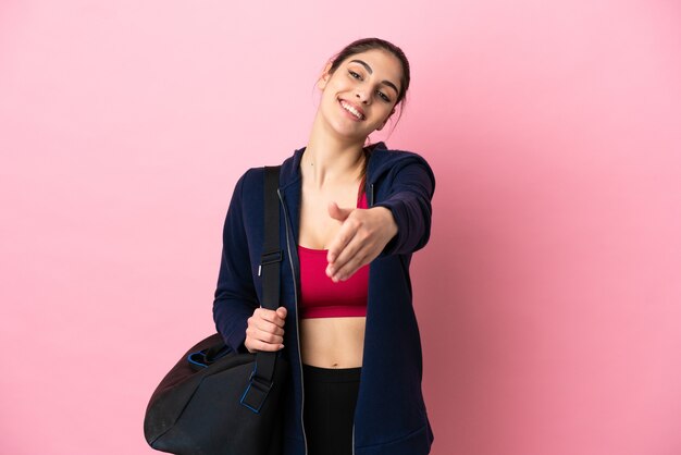 Jeune femme caucasienne sportive avec sac de sport isolé sur fond rose se serrant la main pour conclure une bonne affaire