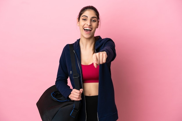 Jeune femme caucasienne sportive avec sac de sport isolé sur un mur rose pointant vers l'avant avec une expression heureuse