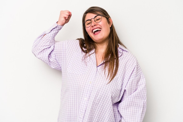 Jeune femme caucasienne en surpoids isolée sur fond blanc célébrant une victoire passion et enthousiasme expression heureuse