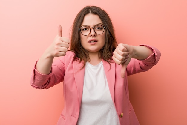 Jeune Femme Caucasienne De Taille Plus Entreprise Montrant Les Pouces Vers Le Haut Et Les Pouces Vers Le Bas, Difficile Choisir