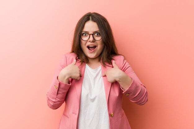 Jeune femme caucasienne de taille plus grande entreprise surpris pointant sur lui-même, souriant largement.