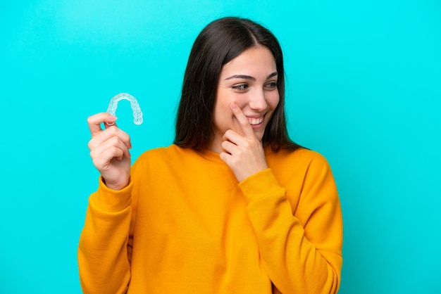 Jeune femme caucasienne tenant des accolades invisibles isolées sur fond bleu pensant à une idée et regardant de côté