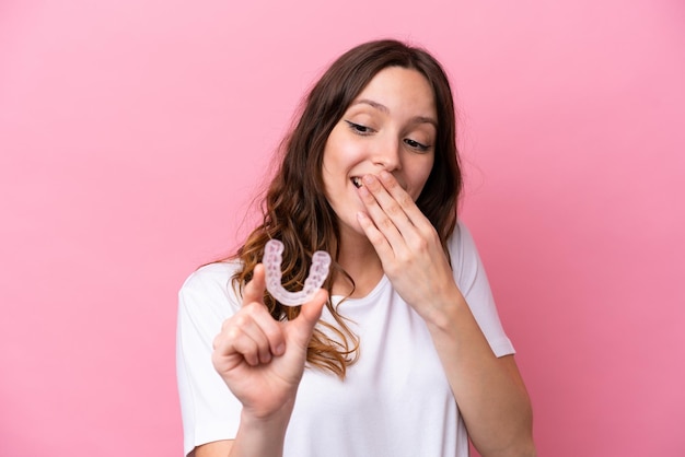 Jeune femme caucasienne tenant des accolades invisibles isolées sur fond rose avec une expression faciale surprise et choquée