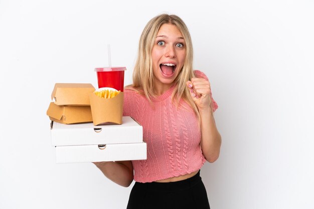 Jeune femme caucasienne tenant des aliments gras isolés sur fond bleu célébrant une victoire en position de gagnant