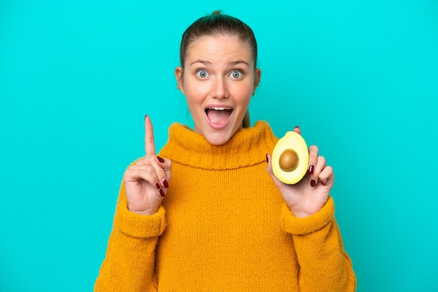 Jeune femme caucasienne tenant un avocat isolé sur fond bleu pointant vers le haut une excellente idée