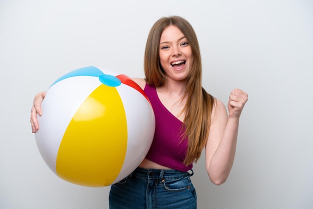 Jeune femme caucasienne tenant un ballon de plage isolé sur fond blanc célébrant une victoire en position de gagnant