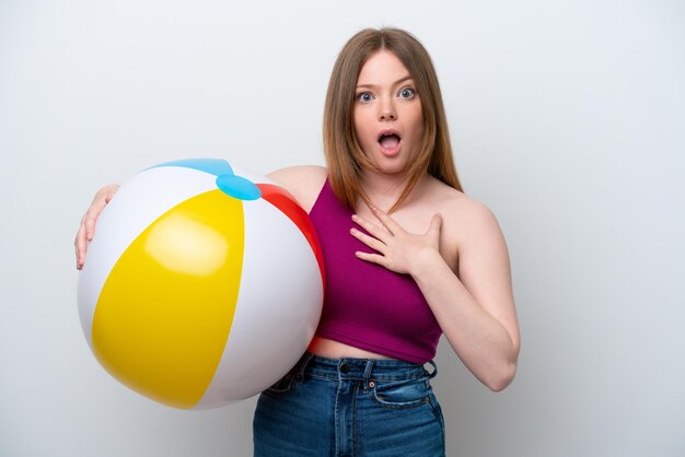 Jeune femme caucasienne tenant un ballon de plage isolé sur fond blanc surpris et choqué tout en regardant à droite