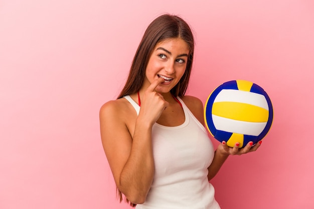 Jeune femme caucasienne tenant un ballon de volley isolé sur fond rose détendue en pensant à quelque chose en regardant un espace de copie.