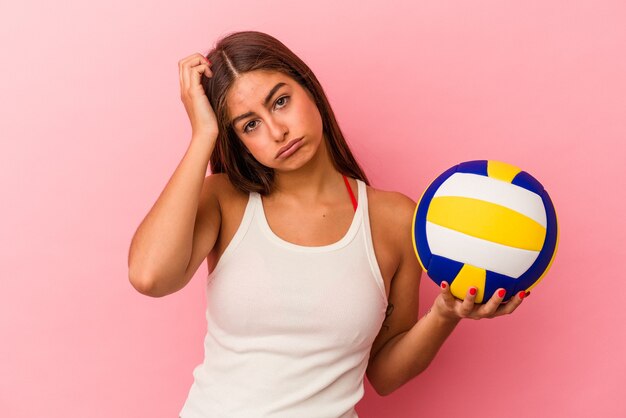 Jeune femme caucasienne tenant un ballon de volley isolé sur fond rose étant choquée, elle s'est souvenue d'une réunion importante.