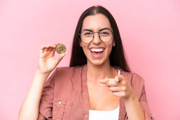 Jeune femme caucasienne tenant un Bitcoin isolé sur fond rose