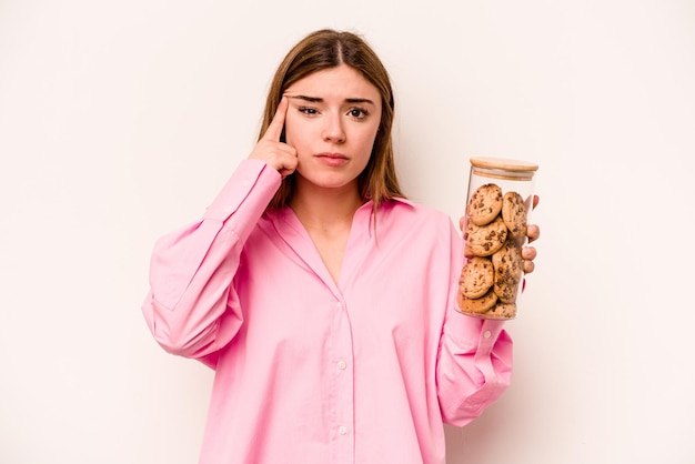 Jeune femme caucasienne tenant un bocal à biscuits isolé sur fond blanc montrant un geste de déception avec l'index