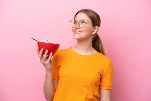 Jeune femme caucasienne tenant un bol de céréales isolé sur fond rose regardant en souriant