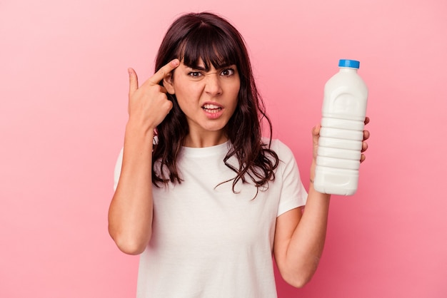 Jeune femme caucasienne tenant une bouteille de lait isolée sur fond rose montrant un geste de déception avec l'index.