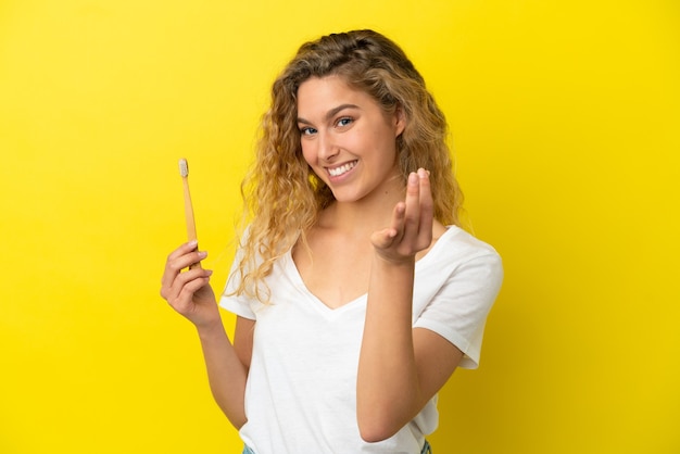 Jeune femme caucasienne tenant un brossage des dents isolé sur fond jaune faisant un geste d'argent