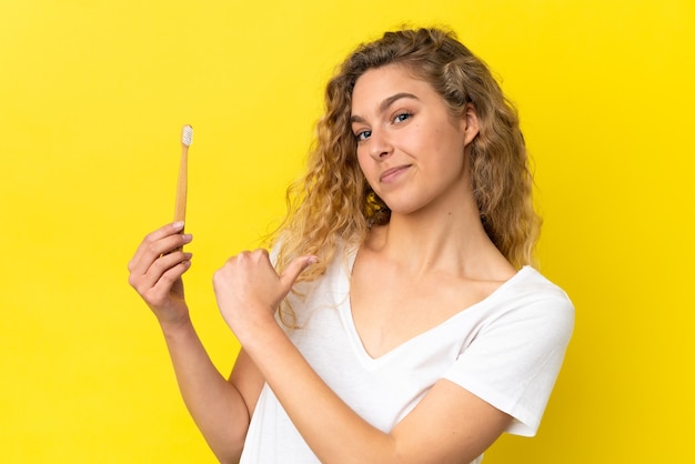 Jeune femme caucasienne tenant un brossage des dents isolé sur fond jaune fier et satisfait de lui-même