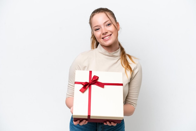 Jeune femme caucasienne tenant un cadeau isolé sur fond blanc avec une expression heureuse